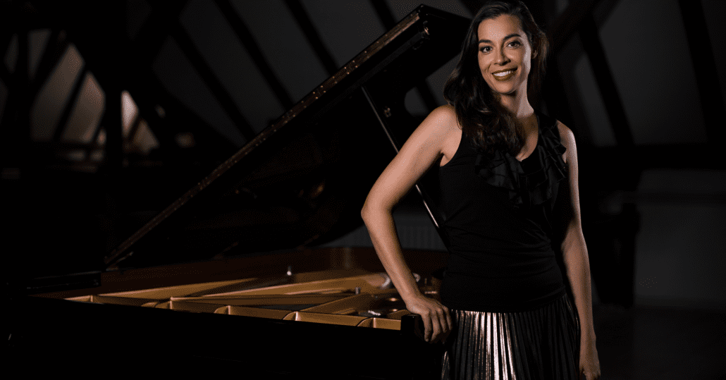 An image of Sibila Konstantinova standing next to a piano.