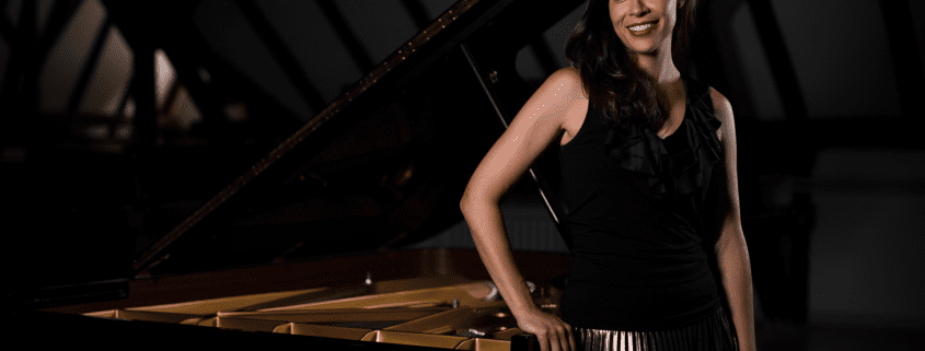 An image of Sibila Konstantinova standing next to a piano.