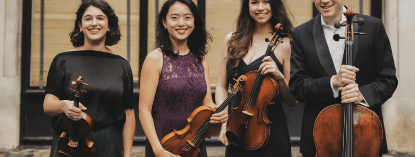 A photo of the Doric String Quartet standing with instruments.